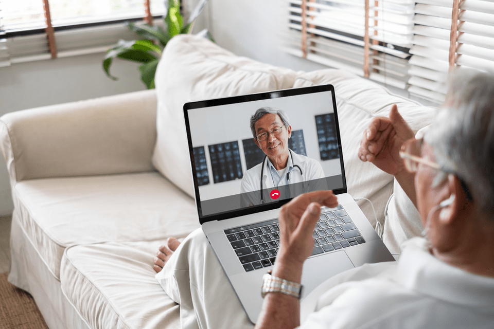Senior man sitting on couch with laptop having a virtual appointment with a doctor.
