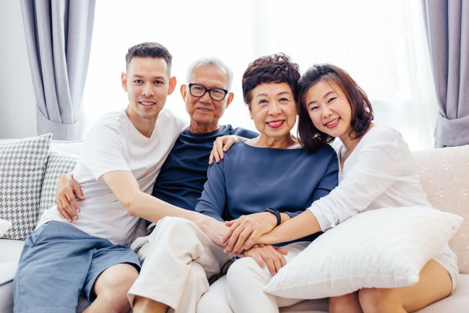 Two adult children embrace their senior parents while sitting on a couch