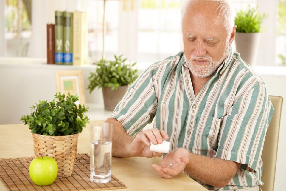 A senior man prepares to take medication after learning about Omeprazole and dementia.