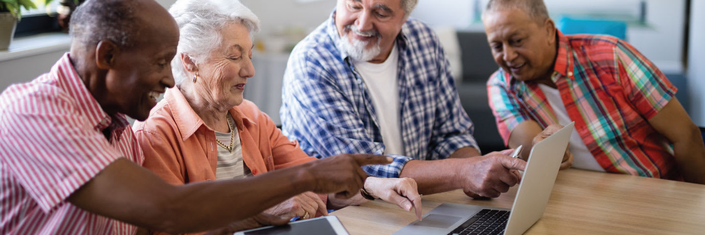 A group of seniors smiling while gathering around a laptop computer