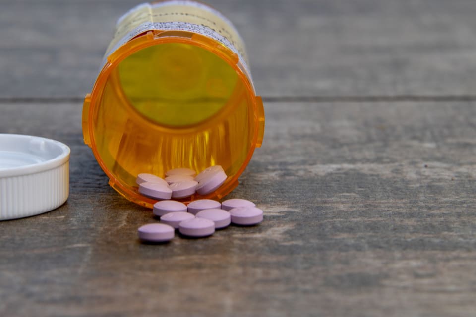 Orange pill bottle laying on its side with pills scattered in front of it.