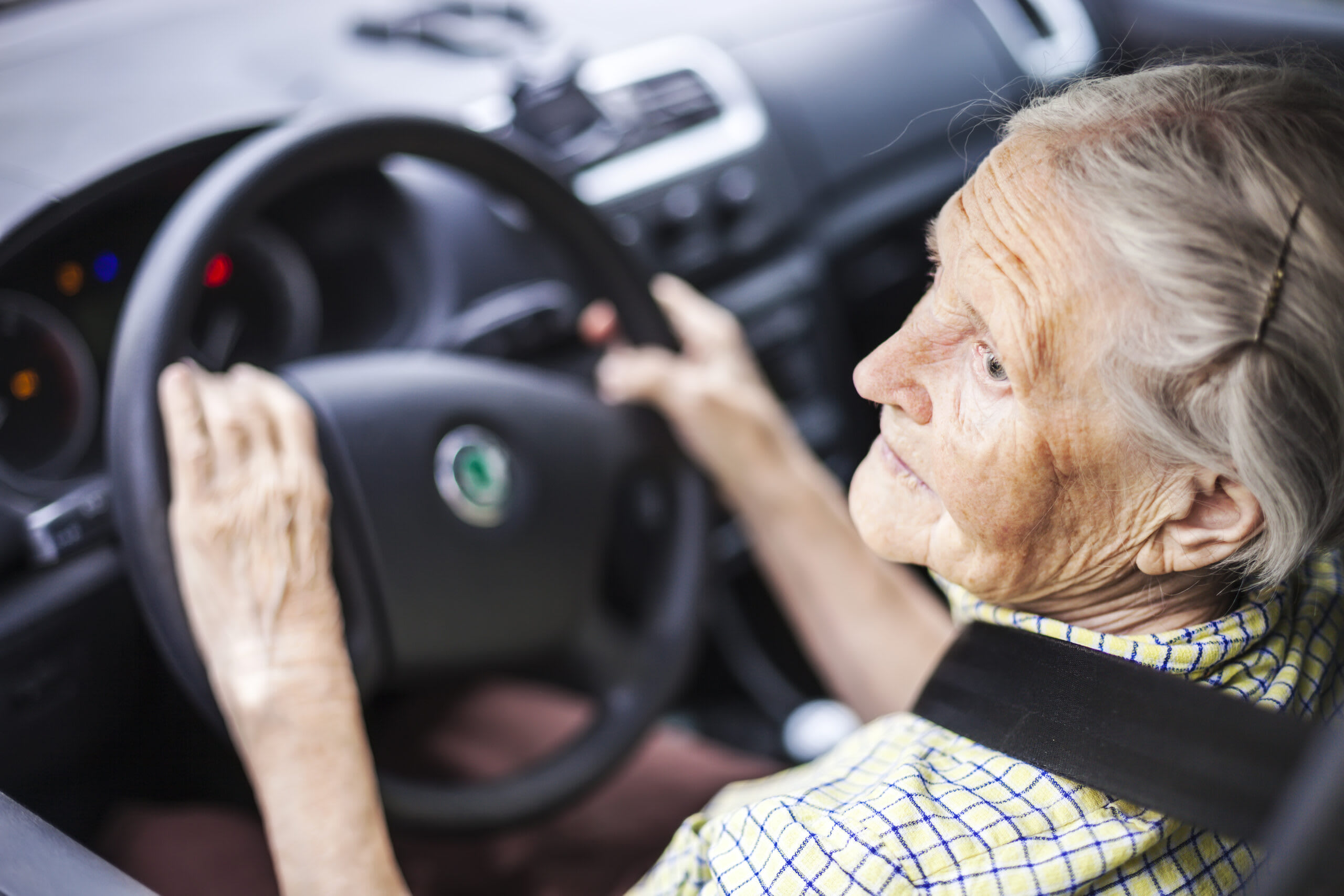 An elderly woman sits at the steering wheel of a car.